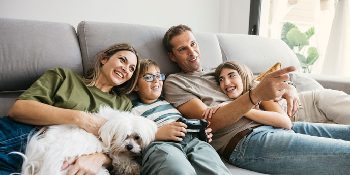 Smiling family of four relaxing on a sofa with their dog, enjoying time together after a life insurance claim helped secure their future