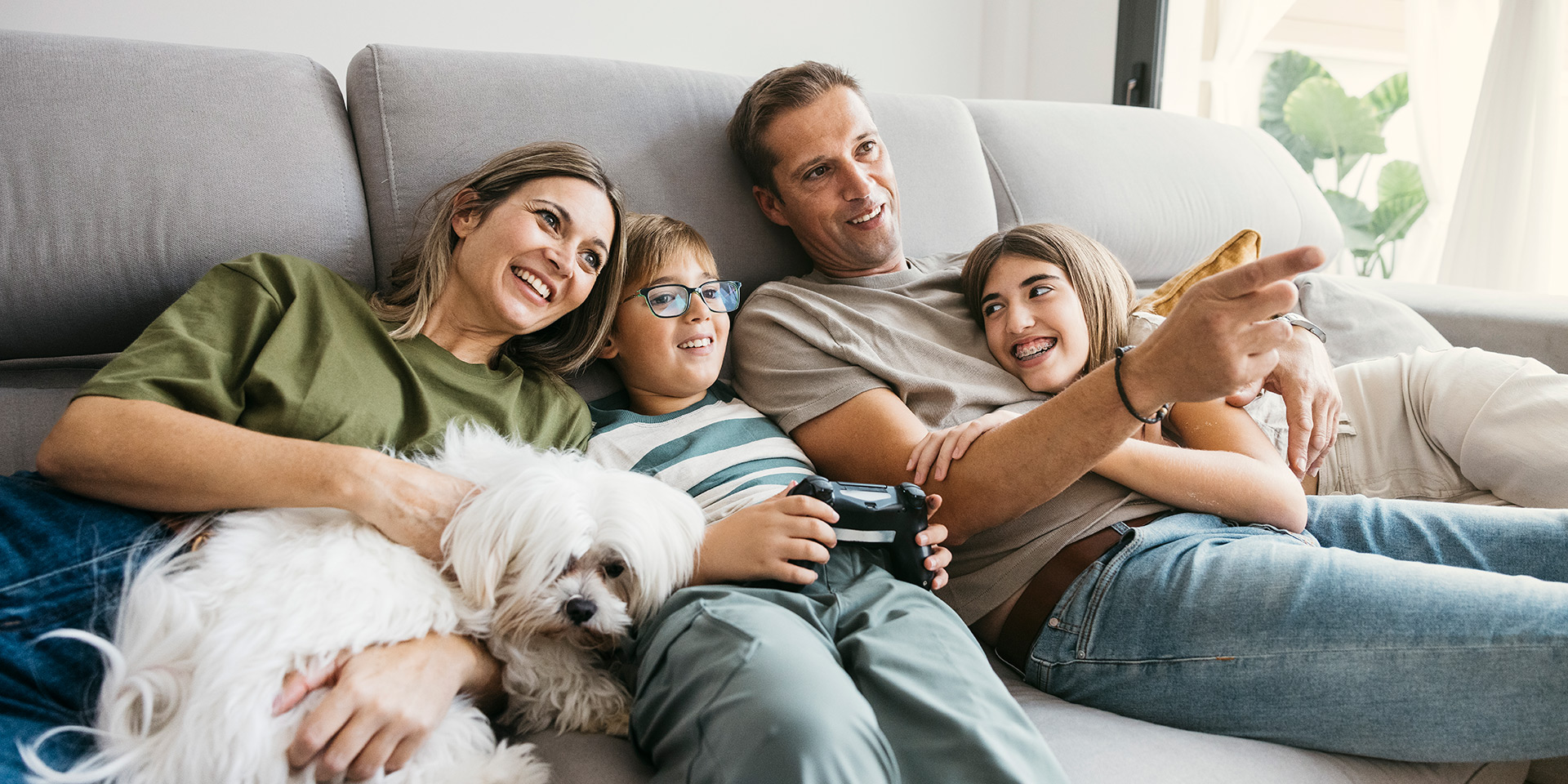 Smiling family of four relaxing on a sofa with their dog, enjoying time together after a life insurance claim helped secure their future.